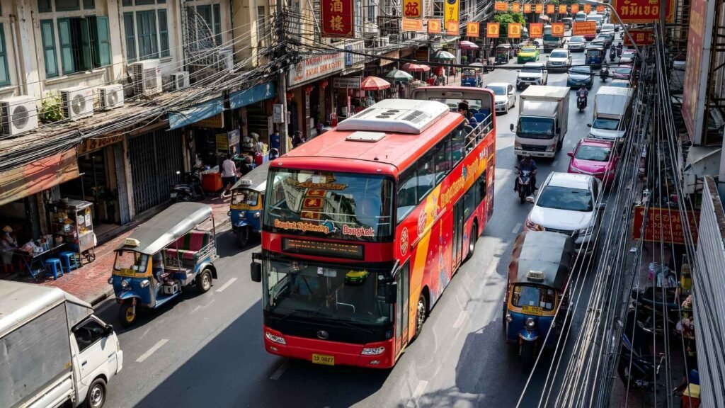 Red double-decker tour bus driving through busy streets of Bangkok Chinatown