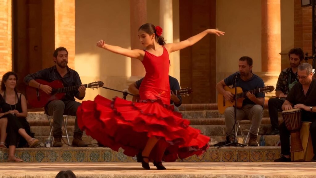 Two beautiful young women with elegant features take a selfie during Feria de Abril in Seville, wearing red and magenta flamenco dresses under golden sunlight.