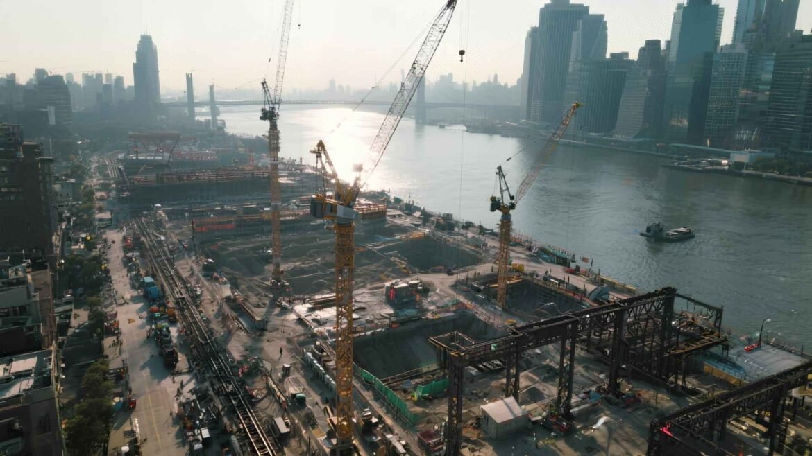 A sunrise aerial view of Manhattan’s Hudson Yards Phase 2 construction area above the Western Rail Yards, showing cranes and foundations near the Hudson River.