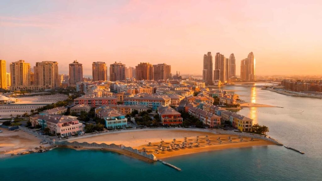 Aerial view of The Pearl Qatar showing colorful villas, marina, turquoise sea, and luxury high-rise towers from an elevated angle.