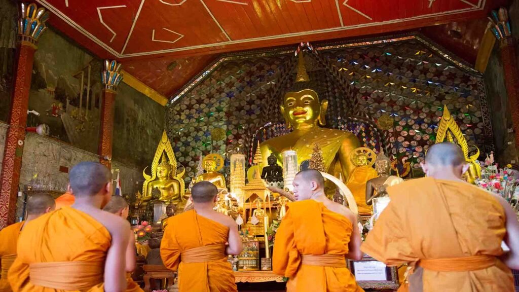 Buddhist monks wearing vibrant orange robes participating in a traditional ritual in Thailand