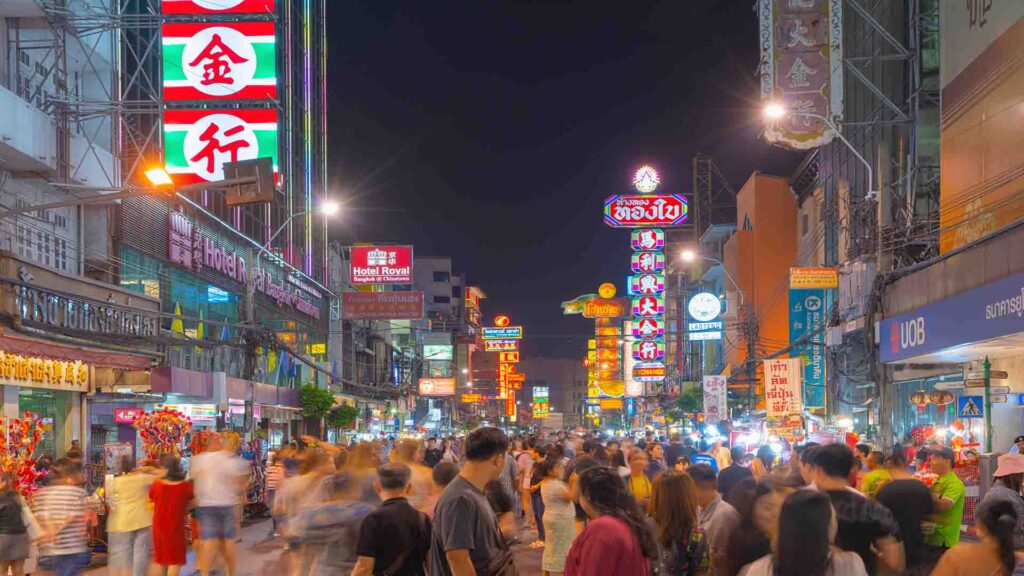Crowds of people walking through Bangkok’s Chinatown streets with busy markets, neon signs, and vibrant urban life