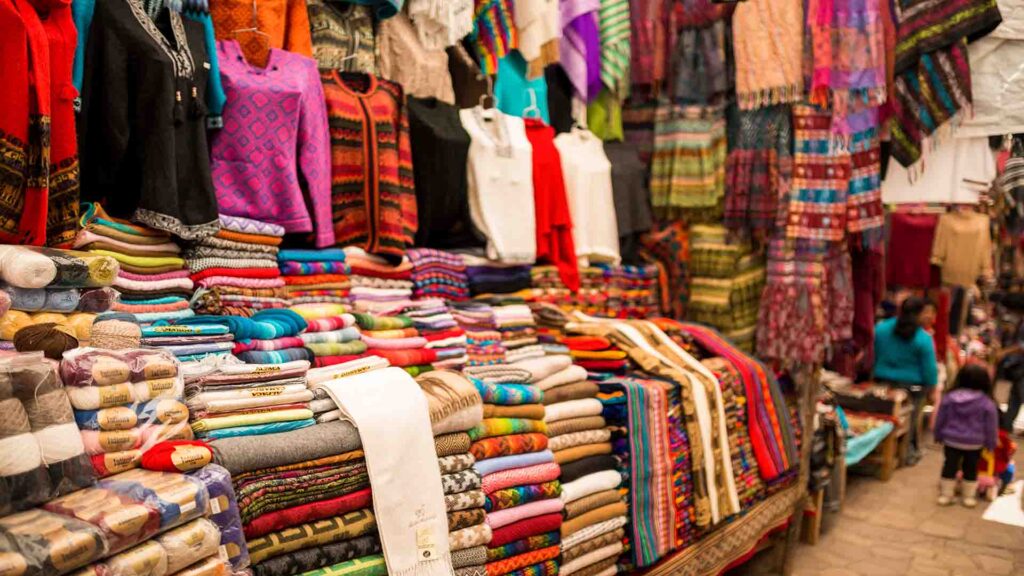 Colorful textile stall with shoppers at a night market, featuring vibrant fabrics, patterned textiles, and lively evening atmosphere