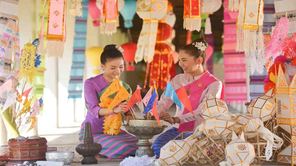 Two women wearing traditional Thai outfits sitting together in a cultural setting in Thailand