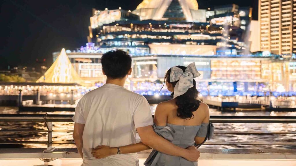 Tourist couple watching a cruise ship pass by along the riverbank in Bangkok, Thailand