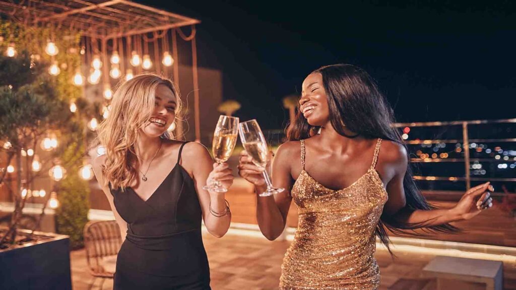 Two beautiful women wearing evening gowns dancing and smiling at an elegant luxury party