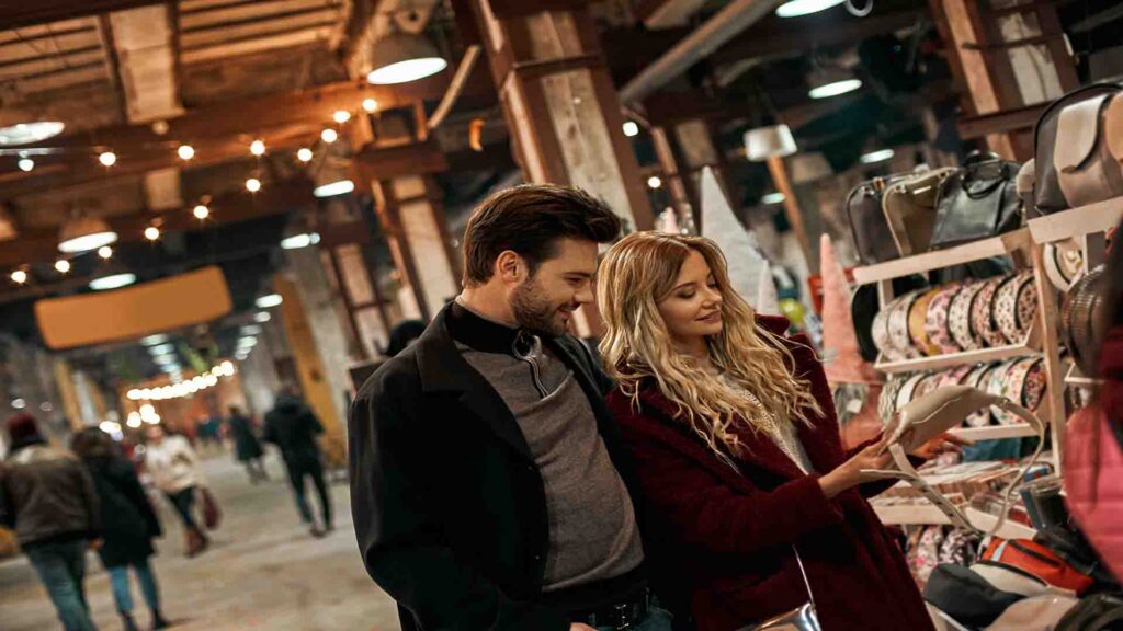 Young couple choosing handmade bags at a small street market, browsing artisanal products in a casual local shopping setting