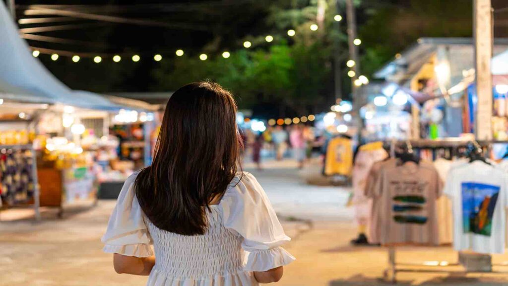 Young woman traveler walking and shopping at a night market with illuminated stalls and a lively evening atmosphere