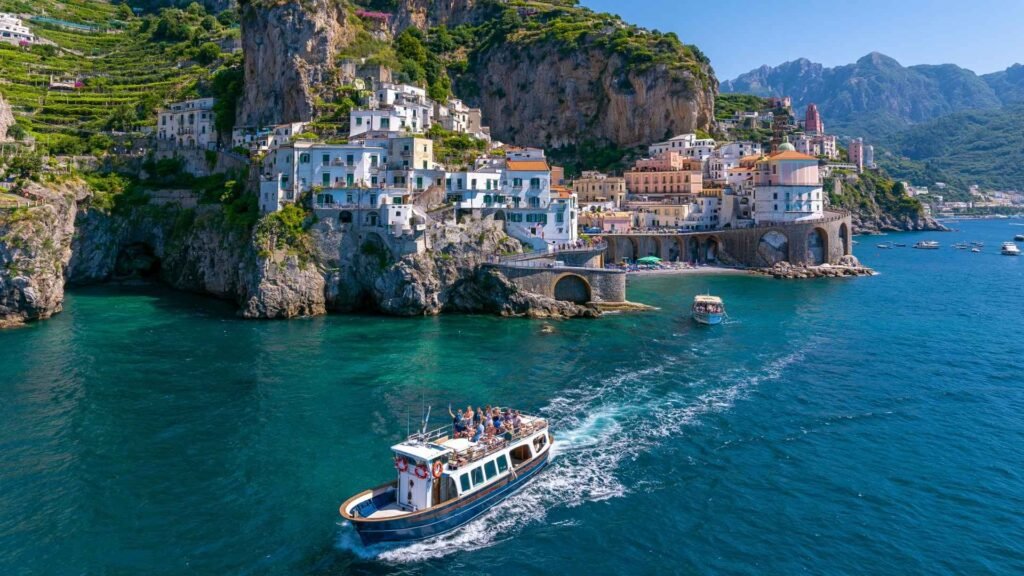 Amalfi Coast cruise boat passing the historic town of Amalfi with colorful coastal buildings and dramatic cliffs viewed from the sea.