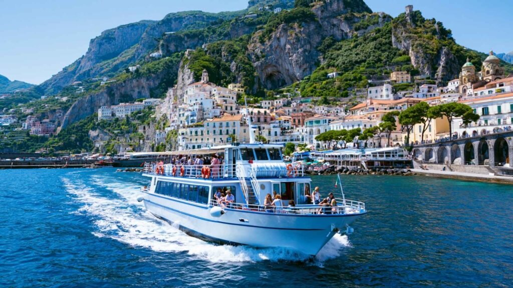 Passenger ferry traveling past Amalfi town on the Amalfi Coast, showing one of the main ways to get around between coastal towns during a 5-day itinerary.