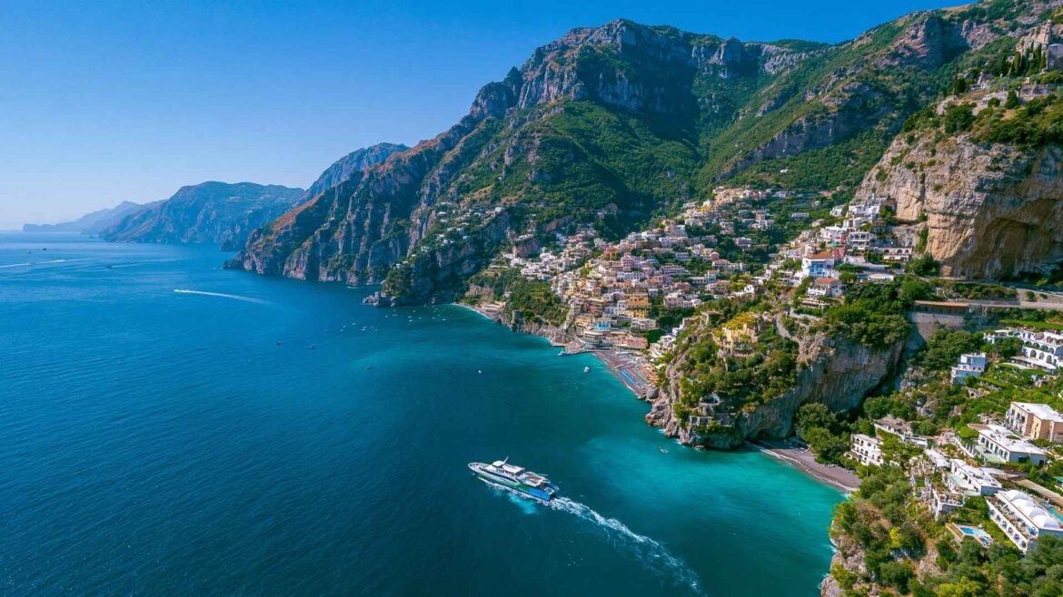 Best Towns to Stay on the Amalfi Coast featuring Positano, dramatic cliffs, turquoise water, and a ferry crossing the coastline.