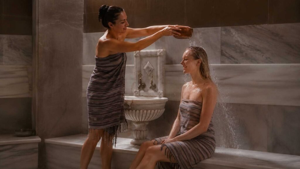 A traditional Turkish bath water ritual at Cağaloğlu Hamamı as warm water is gently poured over a visitor beside a historic marble kurna in Istanbul.