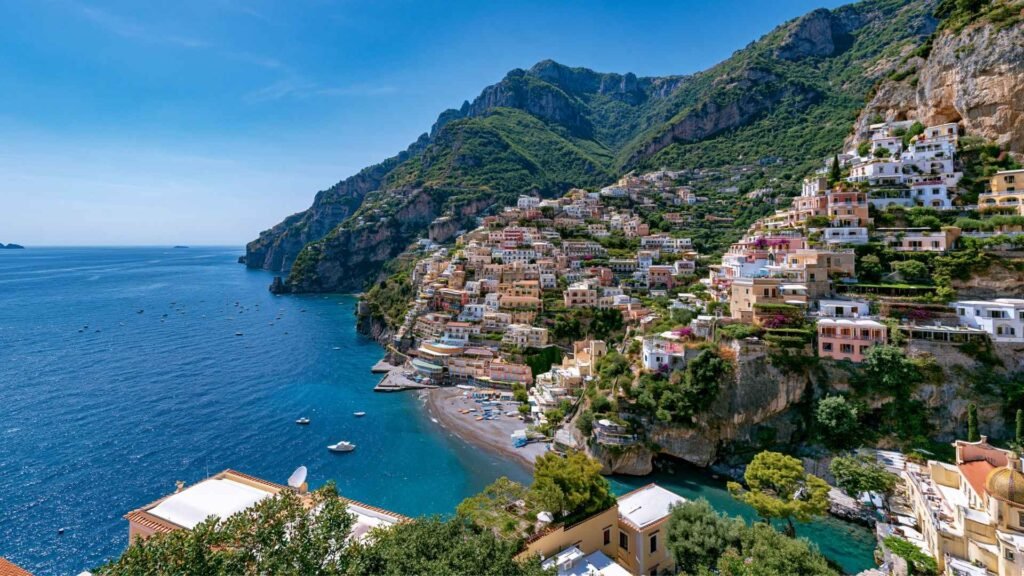 Panoramic view of Positano’s colorful cliffside houses and beach on the Amalfi Coast under bright summer skies.