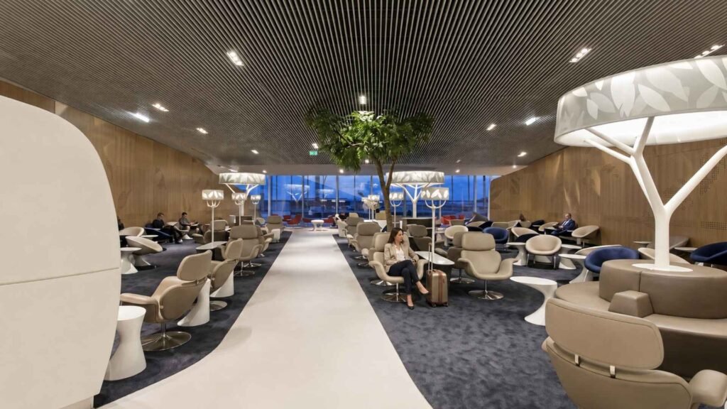 Terminal 2E lounge at Paris CDG with navy and cream seating, sculptural lighting and travellers relaxing beside a central walkway