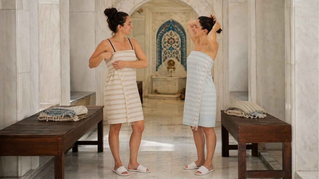 Two women wearing striped peştemals and slippers inside a Turkish bath