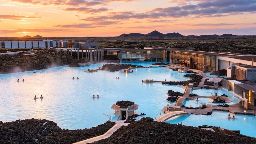 Wide view of Blue Lagoon’s milky-blue water, lava rocks and spa buildings beneath a warm evening sky.