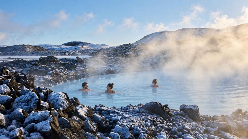 Visitors bathing in Blue Lagoon’s steaming milky-blue water, surrounded by snow-covered lava rocks in winter.