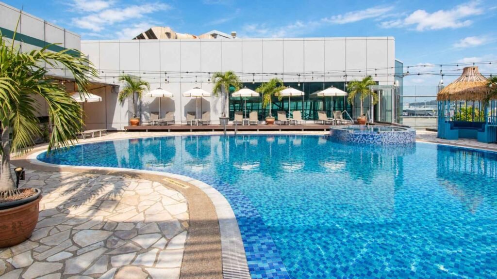 Outdoor swimming pool and raised circular jacuzzi at Changi Transit Hotel T1, surrounded by palm trees and poolside loungers.