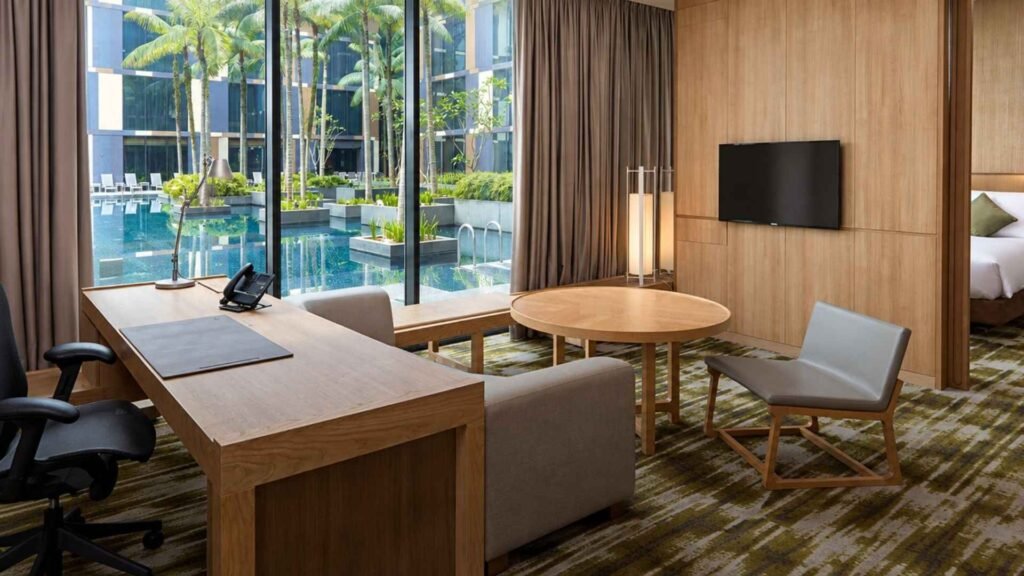 Crowne Plaza Changi Airport suite with a wooden desk, lounge seating and floor-to-ceiling windows overlooking the pool.