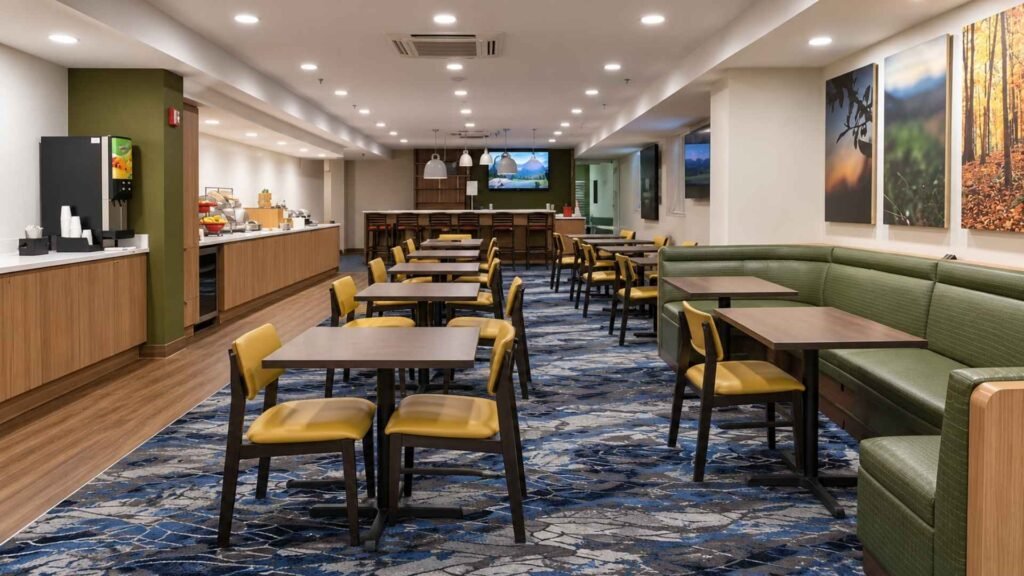 Fairfield Inn JFK breakfast area with yellow chairs, green upholstered seating and a buffet counter.