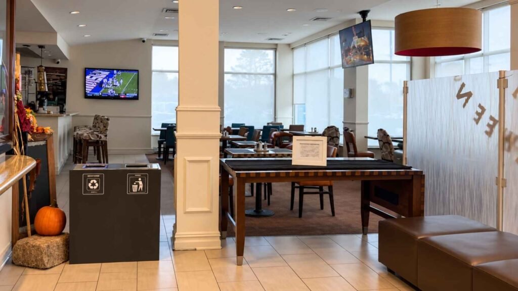 Hilton Garden Inn JFK shared seating area with dining tables, large windows and a brown upholstered bench.