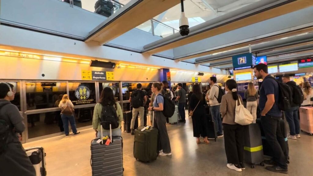 Travellers with suitcases waiting beside the glass platform doors at a JFK AirTrain station.