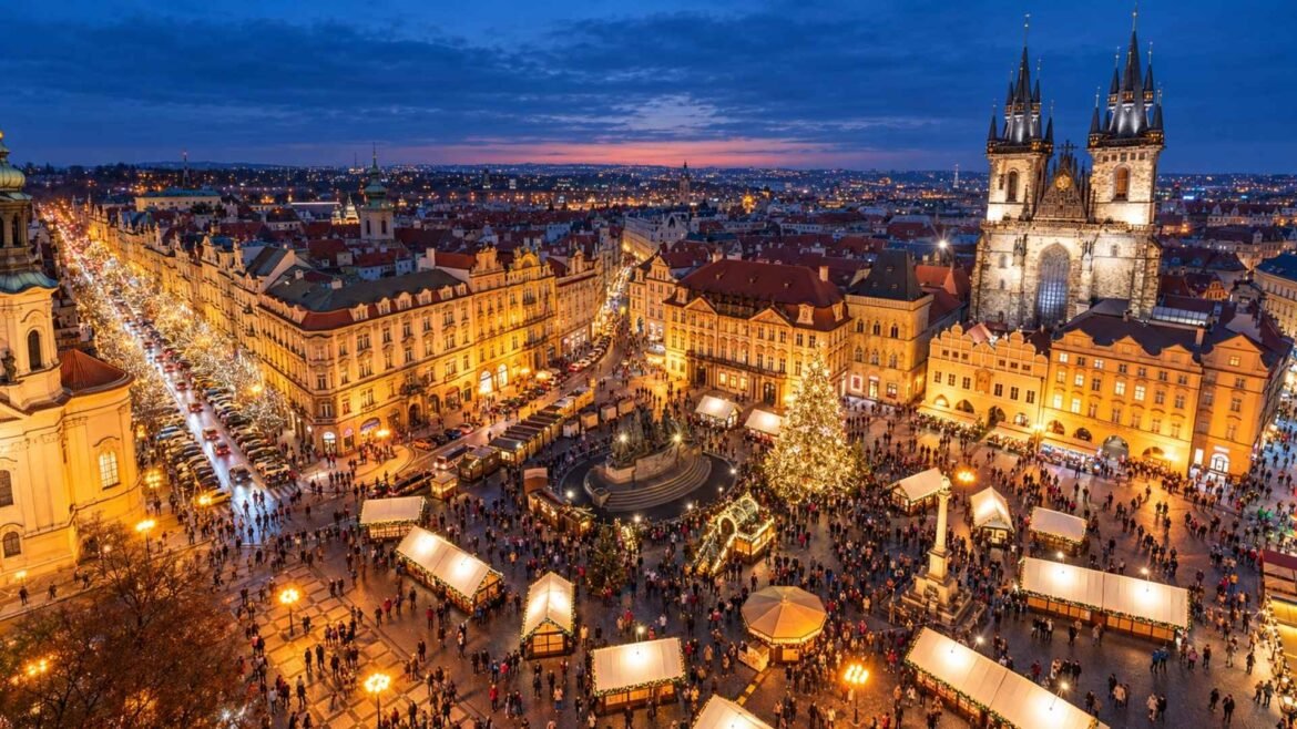 Prague Christmas markets in Old Town Square at dusk, with illuminated stalls, a Christmas tree and the twin towers of Týn Church.