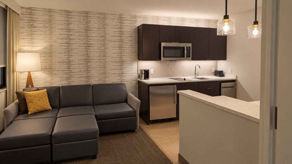 Residence Inn JFK suite with a kitchenette, grey sofa, ottoman and white breakfast counter.